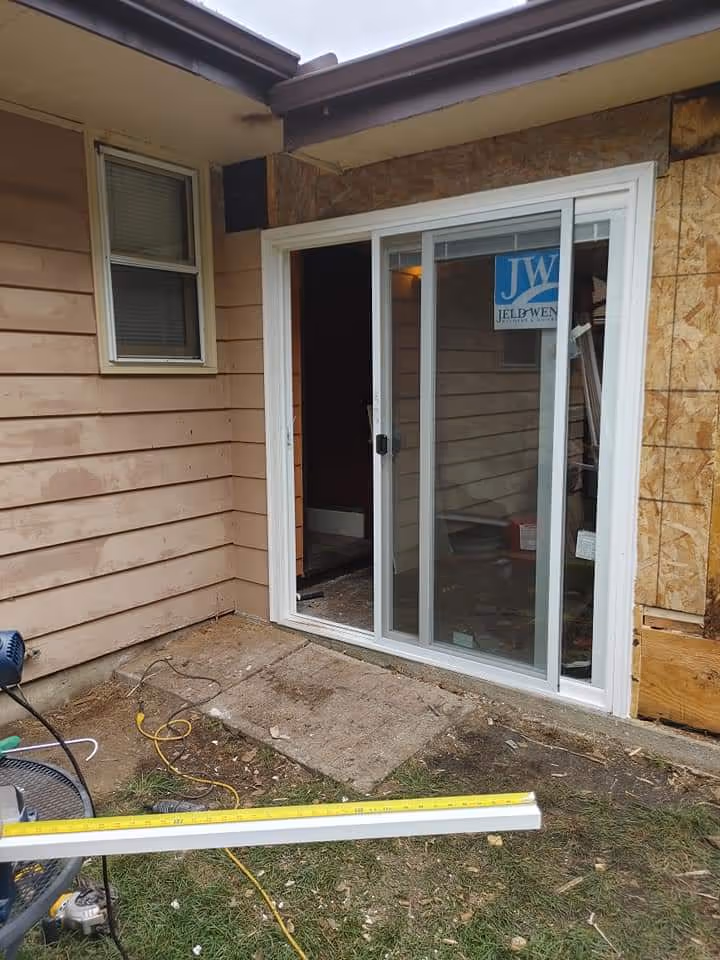 Partially constructed patio area outside a sliding glass door with construction materials and tools nearby.