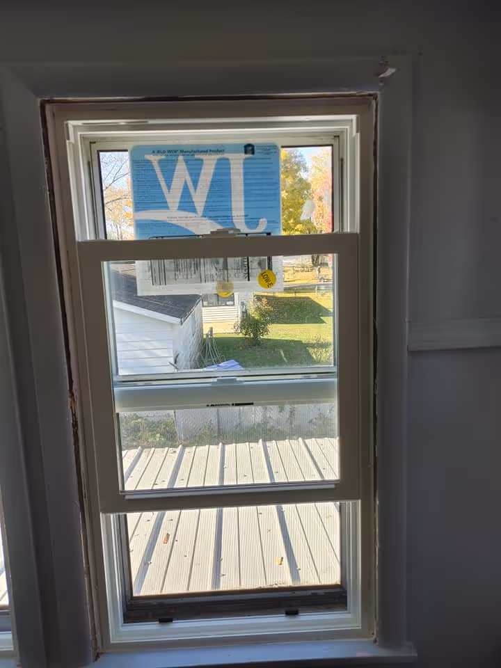 New white double-hung window installed showing a backyard with a deck, grass, and a small white shed.