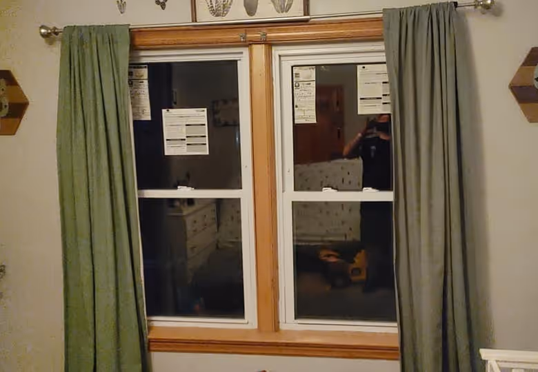 Wood framed double window with green curtains on both sides and stickers on the glass panes in a beige room.